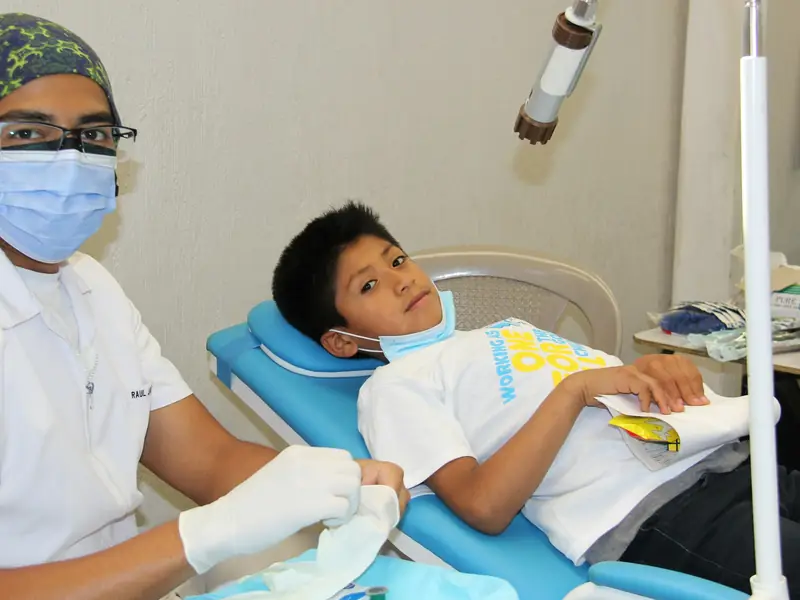 Dentista revisando los dientes de un niño latino gracias a su seguro dental