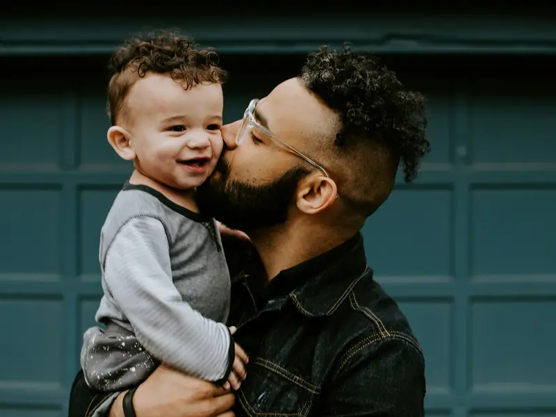 Padre latino besando a su bebé, protegido por su seguro de vida en USA